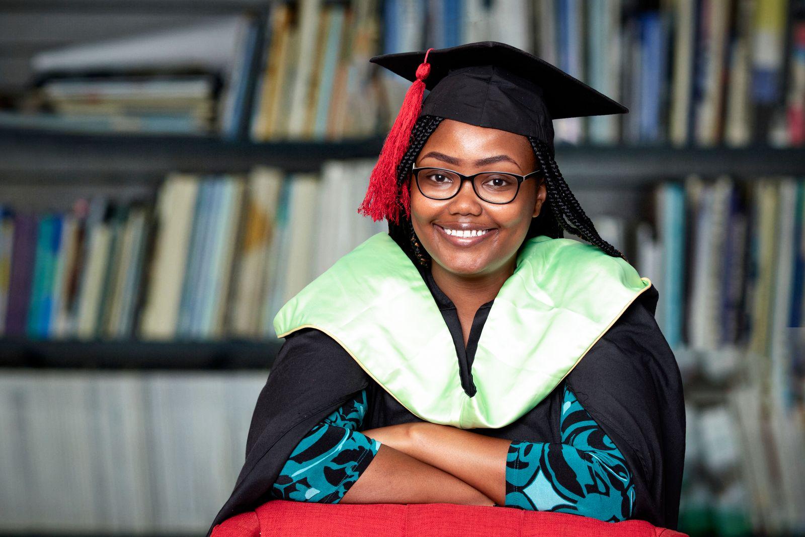 A graduate in cap and gown smiling in a university library